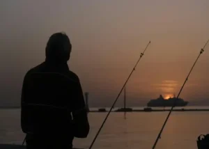 Deens Vissen voor Beginners: Een man die s'avonds aan het vissen als een beginnen in Denemarken met een boot op de achtergrond.